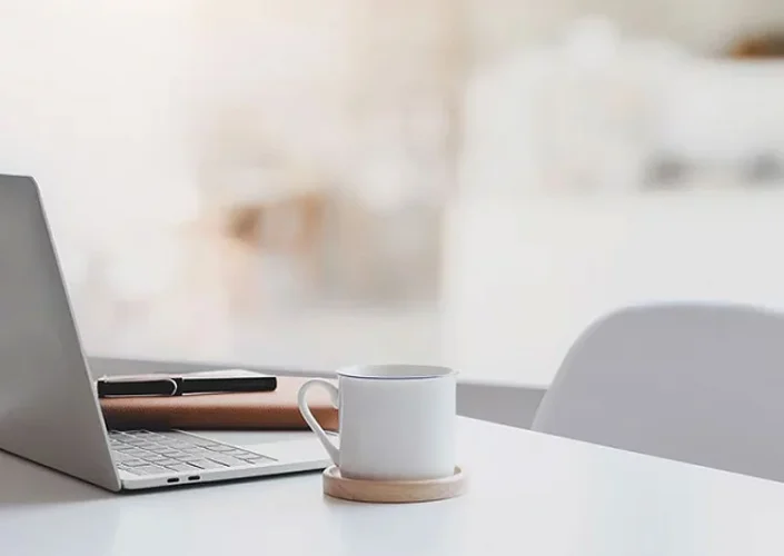 Laptop, Tasse und Notizbuch auf einem Schreibtisch, symbolisiert einen modernen Arbeitsplatz in einer Marketingagentur. 